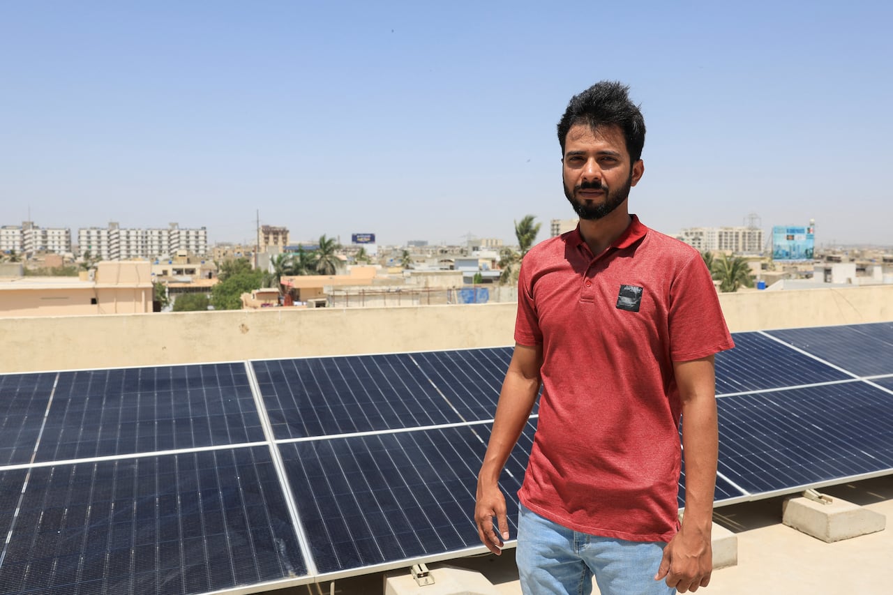 A man poses with solar panels on a city roof with an apartment building in the background