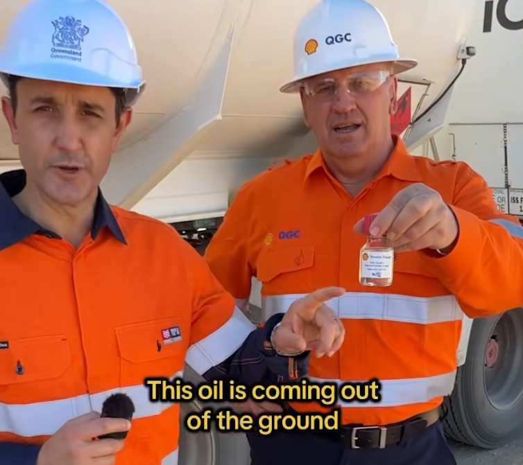 Two men in high-viscosity vests hold oil samples next to an oil tanker.