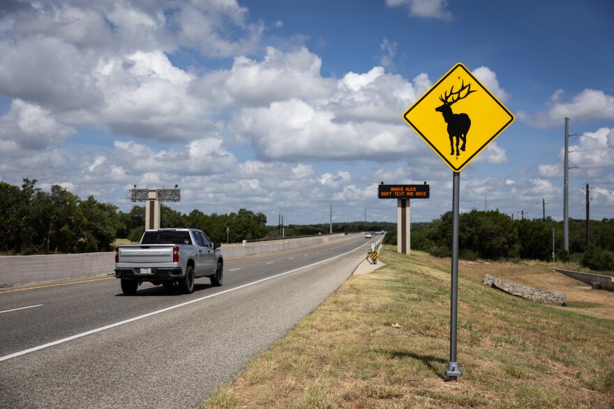 A photo of a yellow animal crossing road sign with a picture of a moose stands beside the highway.